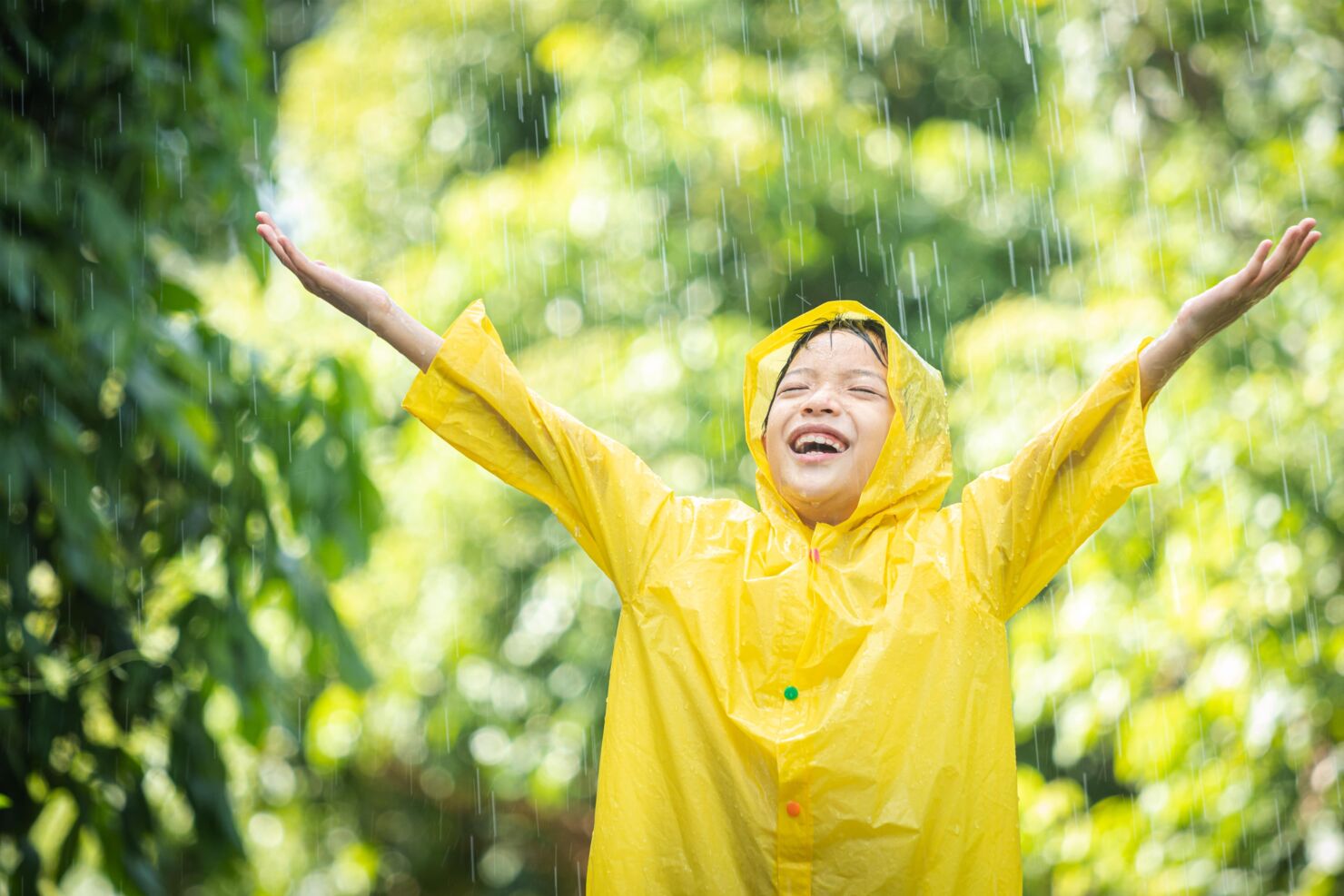 Kind trägt eine Regenjacke und geniesst den Regen