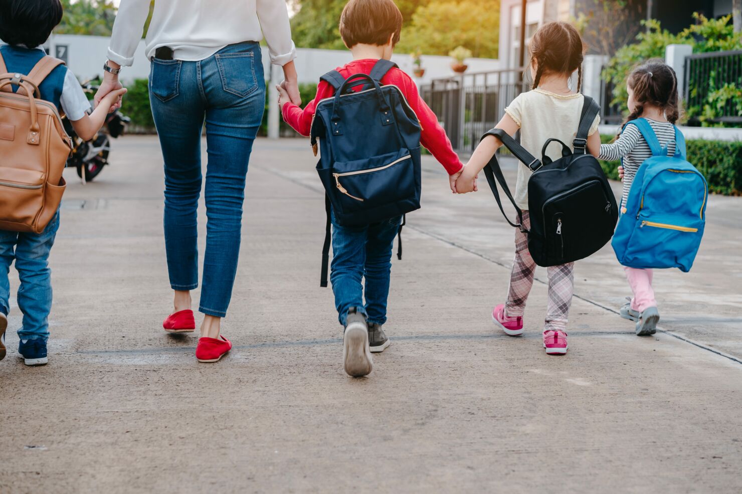 Es werden vier laufende Kinder mit einer Mutter Hand-in-Hand zusammen zur Schule geführt