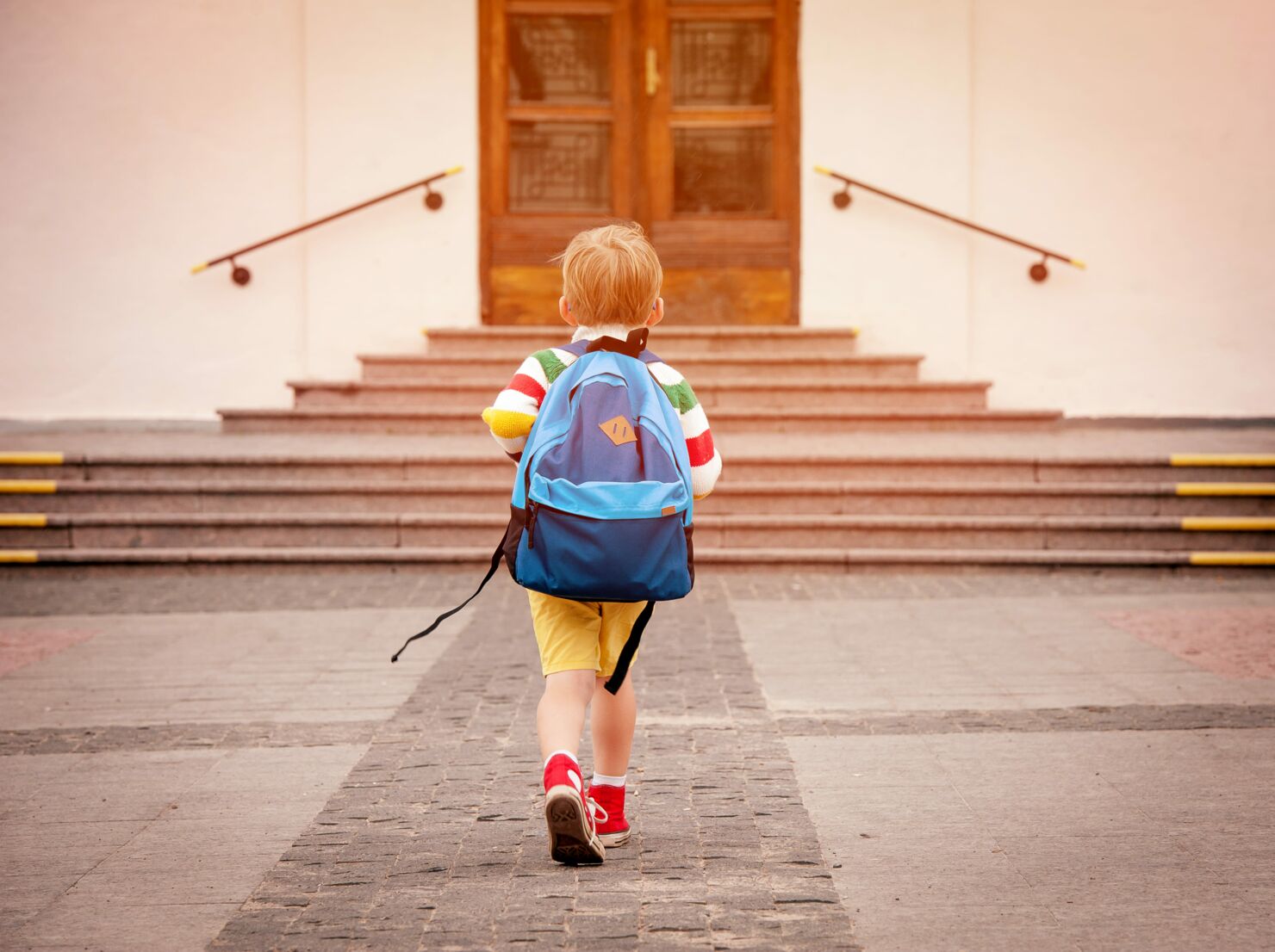 Ein Kind lauft mit einem Rucksack zu Treppen eines Hauses zu