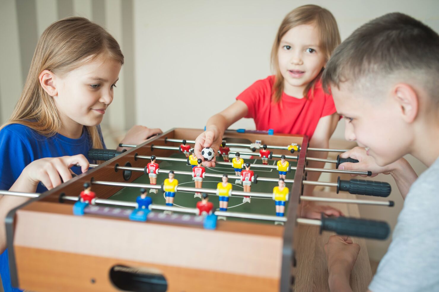 An einem Tischkicker spielen 3 Kinder konzentriert