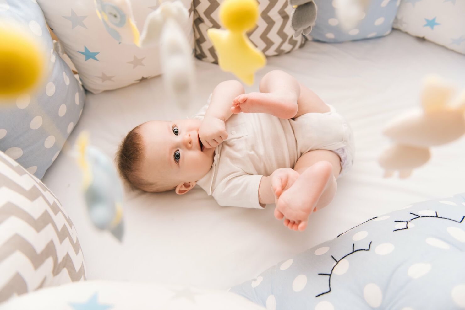 Baby liegt im Kinderbett und spielt mit den Füssen und Händen