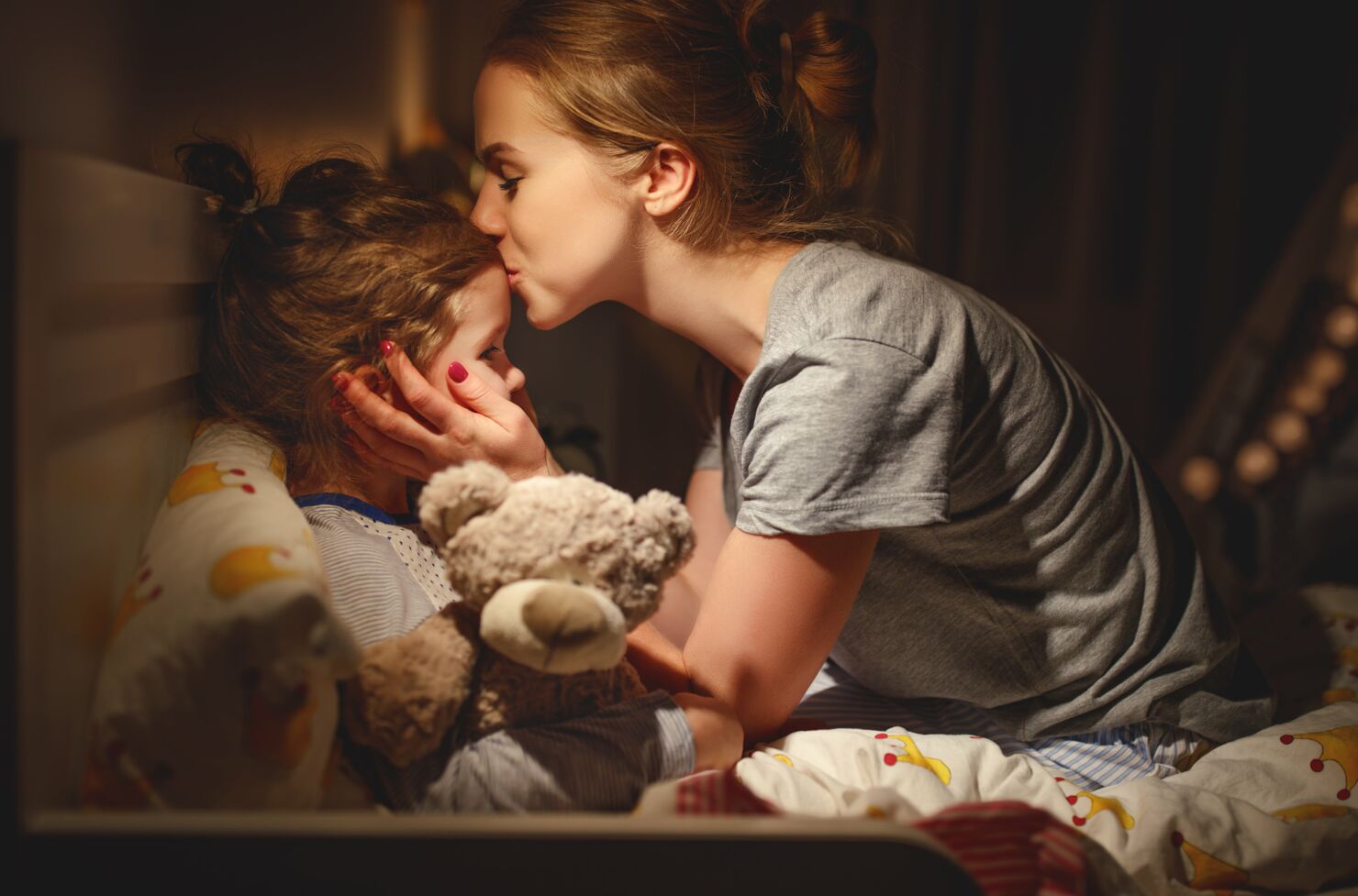 Die Mutter gibt ihrer Tochter vor dem Einschlafen einen Kuss auf die Stirn